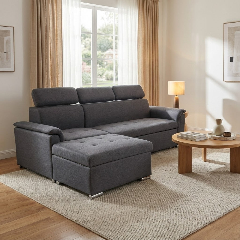Elegante salotto dai toni neutri con il divano Derrick grigio scuro, pouf frontale e tavolino rotondo in legno.