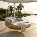 Divano letto sospeso Formosa in rattan intrecciato con cuscini beige e azzurri, installato sotto un pergolato a bordo piscina.