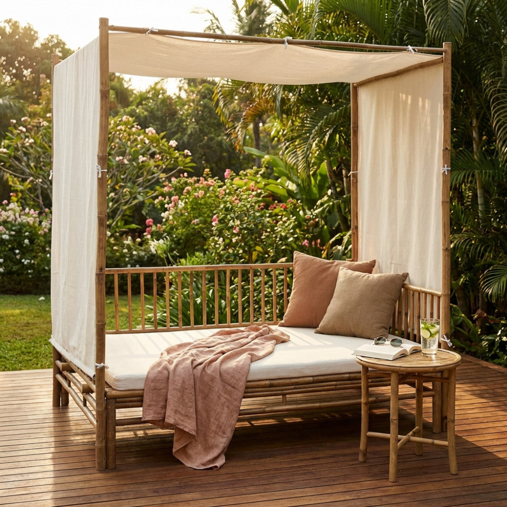 Divano letto Manhattan in legno marrone con baldacchino e tessuti chiari, ambientato in un giardino tropicale al tramonto.