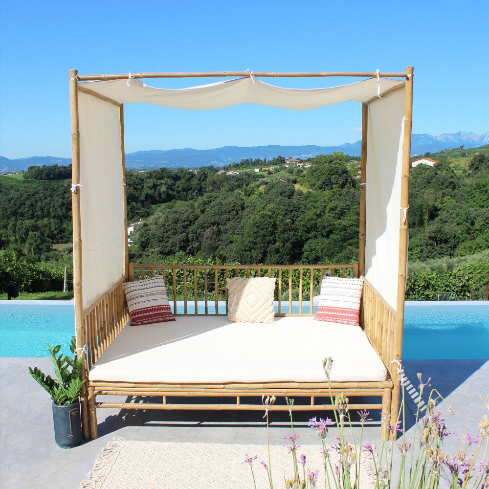 Divano letto Manhattan in legno allestito a bordo piscina con cuscini decorativi, affacciato su un paesaggio collinare.