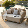 Divano Mendoza a due posti in poliestere beige, posizionato a bordo piscina al tramonto con cuscini decorativi.