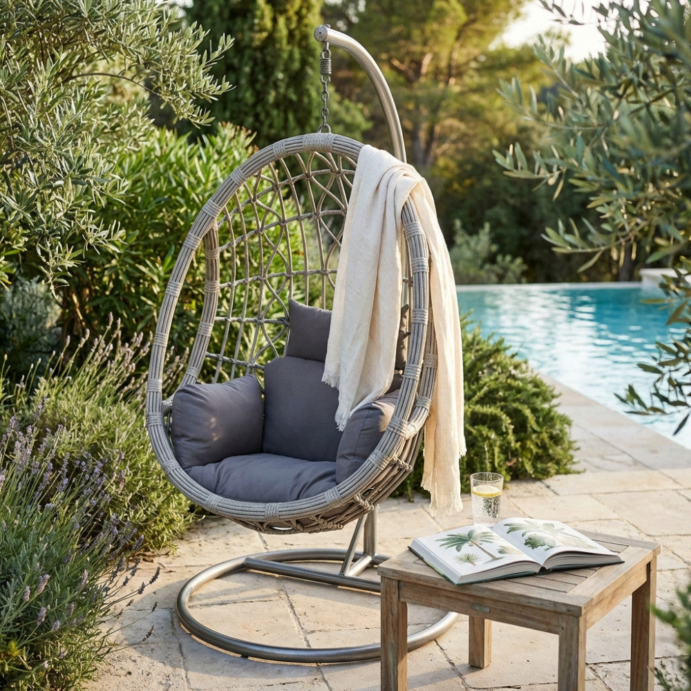 Vista angolare del dondolo sospeso Capraia immerso nel verde del giardino, con un morbido plaid appoggiato sulla seduta.