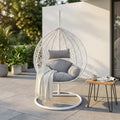 Dondolo Giglio in wicker bianco con cuscini grigi, ambientato su un patio moderno illuminato dal sole.