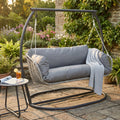 Dondolo a 2 posti Glasgow in metallo antracite inserito in un rigoglioso giardino con tavolino laterale.