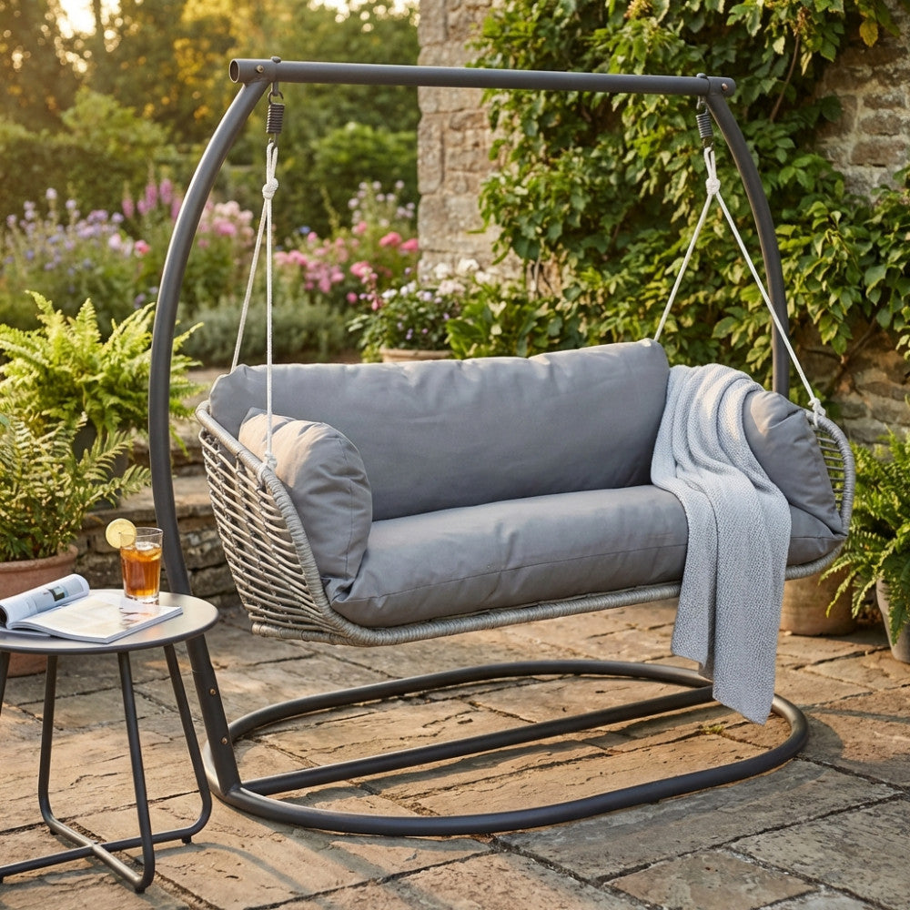 Dondolo a 2 posti Glasgow in metallo antracite inserito in un rigoglioso giardino con tavolino laterale.