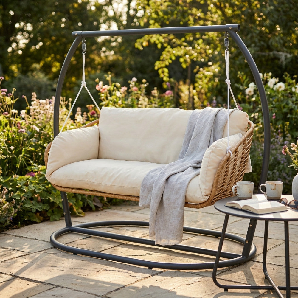 Dettaglio del dondolo moderno Glasgow con cuscini beige e coperta in lino su un patio in pietra.