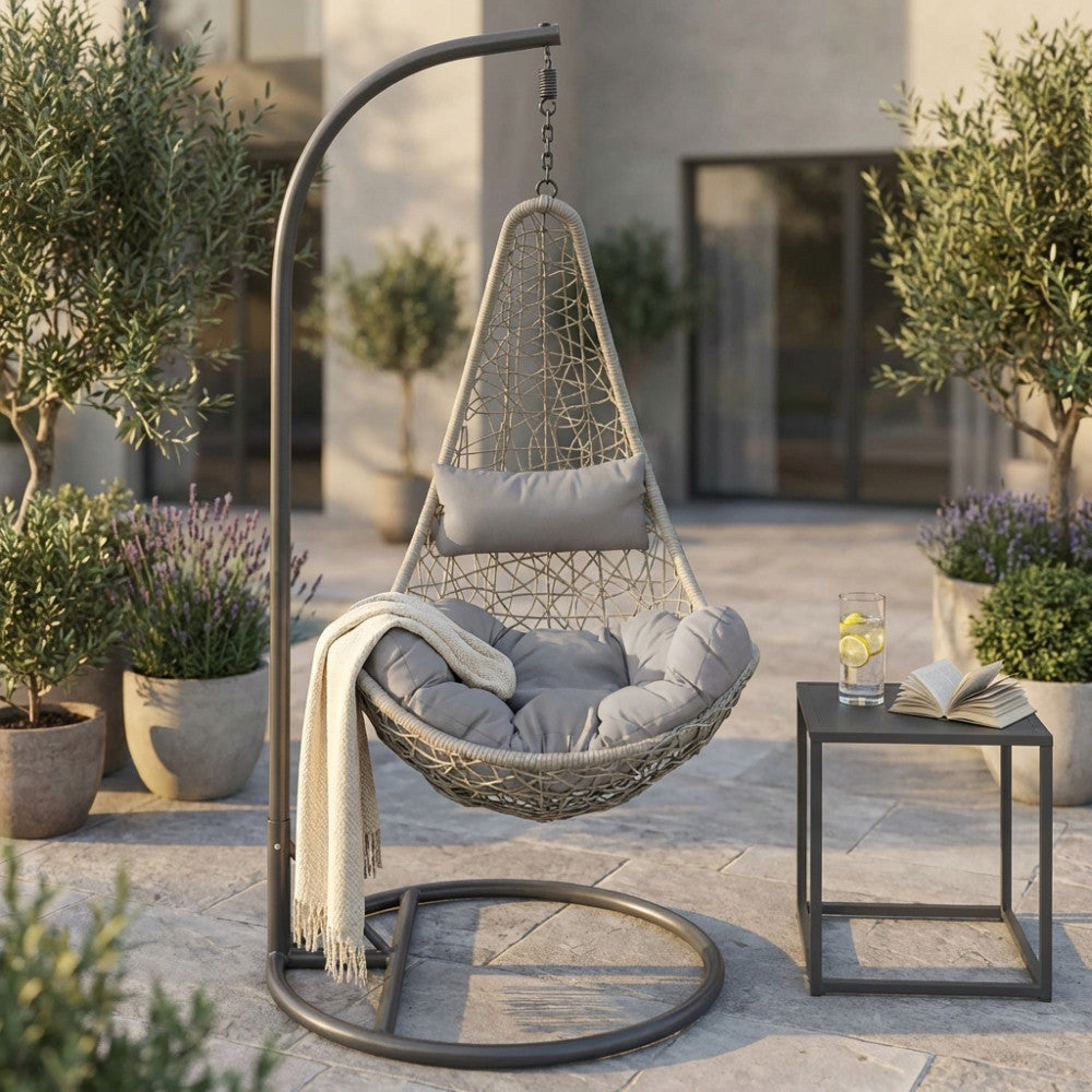 Vista frontale del dondolo Ponza sospeso, ambientato in un cortile elegante con tavolino minimalista e piante decorative.