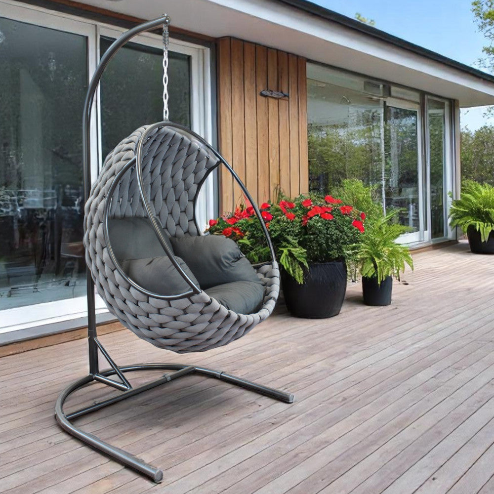 Poltrona a uovo sospesa posizionata su una terrazza in legno vicino a grandi vetrate e piante.
