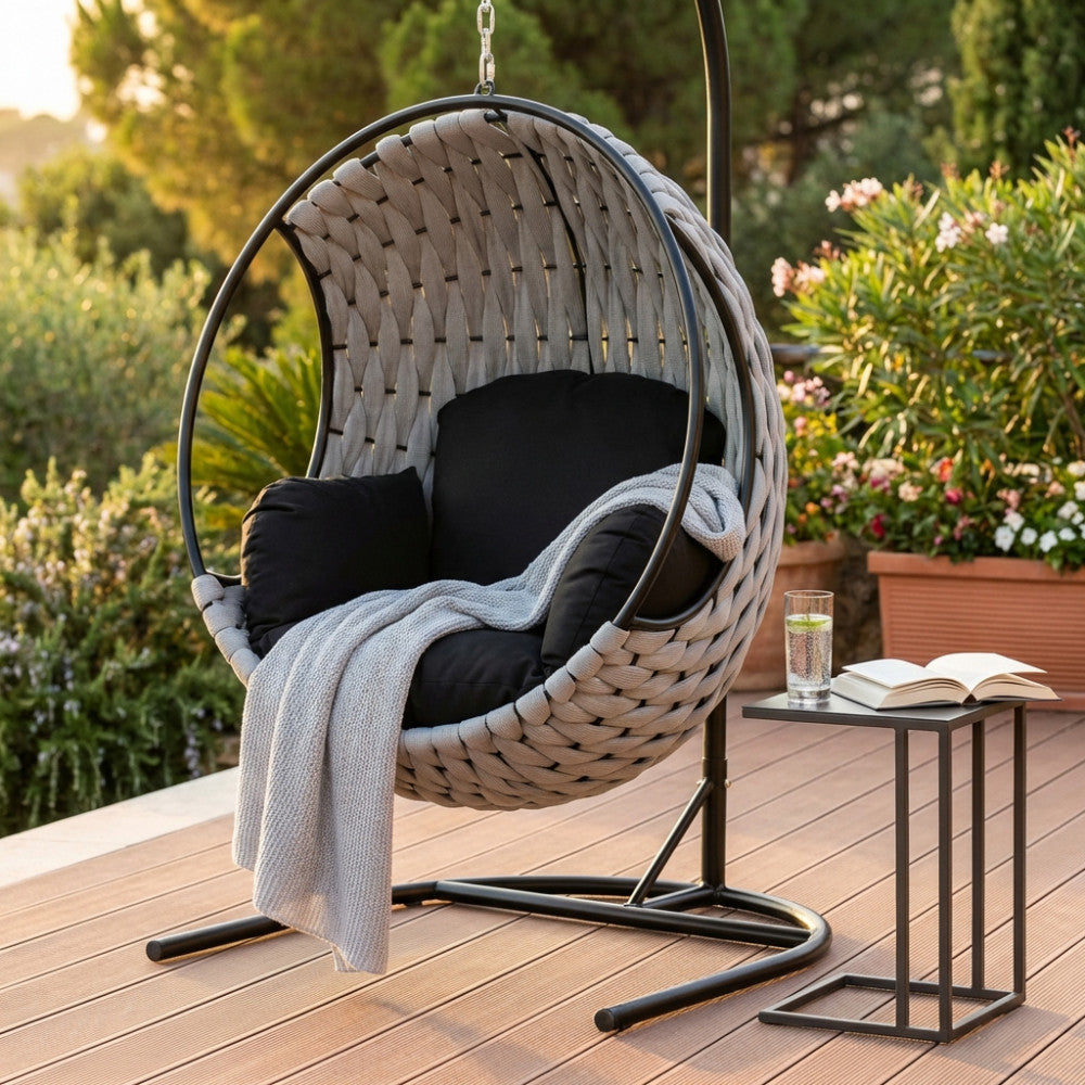 Poltrona sospesa Spargi in polipropilene grigio chiaro allestita su una terrazza in legno con tavolino moderno.