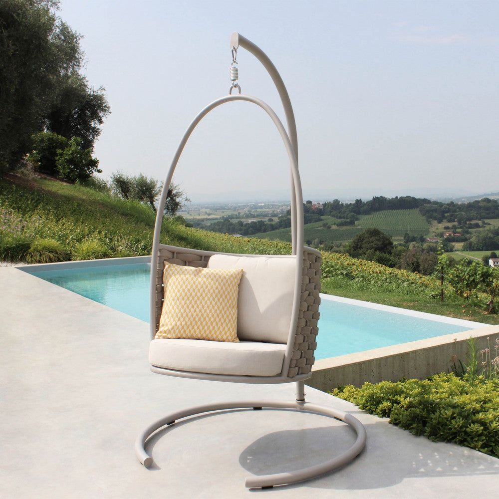 Dondolo sospeso posizionato a bordo piscina con vista panoramica sulle colline, arricchito da un cuscino decorativo giallo.