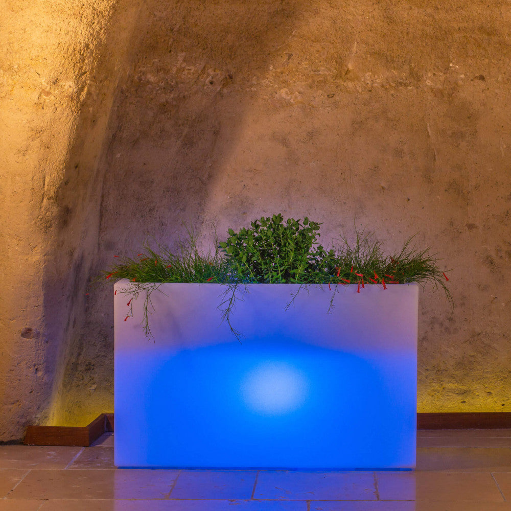 Fioriera luminosa Sculptor 50 accesa con un vibrante LED blu, incastonata in una suggestiva architettura in pietra rustica.