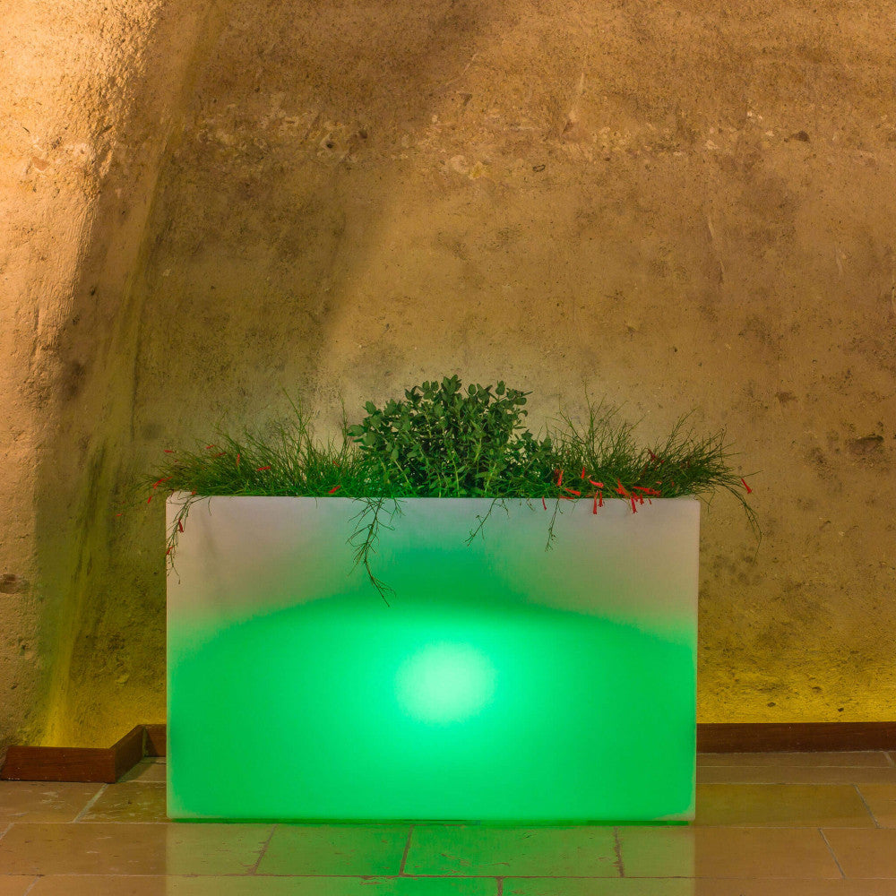 Fioriera Sculptor 50 che emette una luce LED verde smeraldo, creando un contrasto cromatico affascinante contro una parete in tufo.