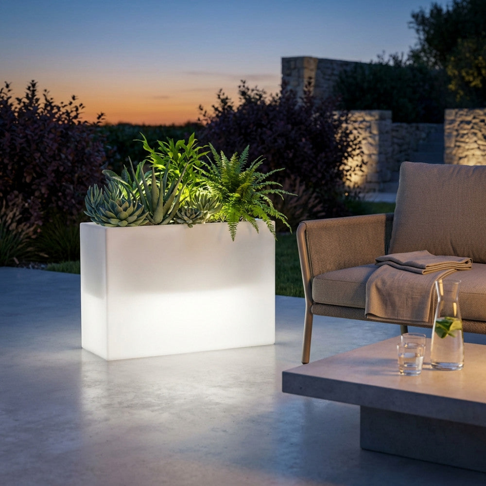 Fioriera luminosa rettangolare in polipropilene bianco con piante grasse e felci, posizionata su un patio moderno al tramonto.