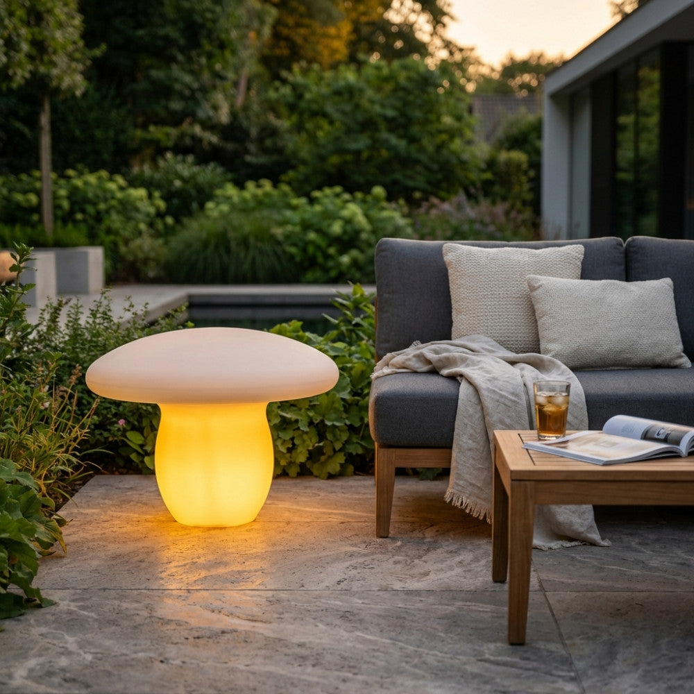 Lampada moderna luminosa posizionata su un patio in pietra vicino a un divano scuro e un tavolino in legno.