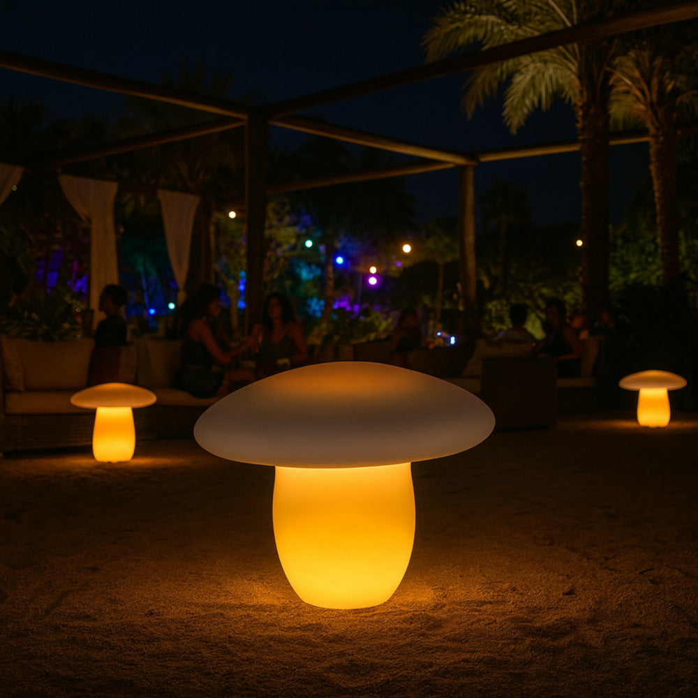 Atmosfera notturna in un'area lounge all'aperto sulla sabbia, illuminata da diverse lampade a fungo gialle.