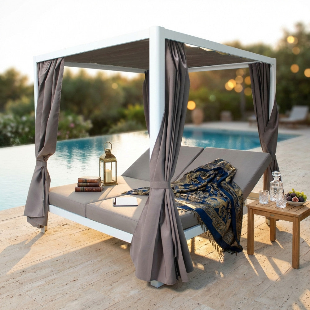 Vista frontale del Gazebo Letto Timbuktu al tramonto, allestito con cuscini decorativi, un plaid blu e accessori eleganti.