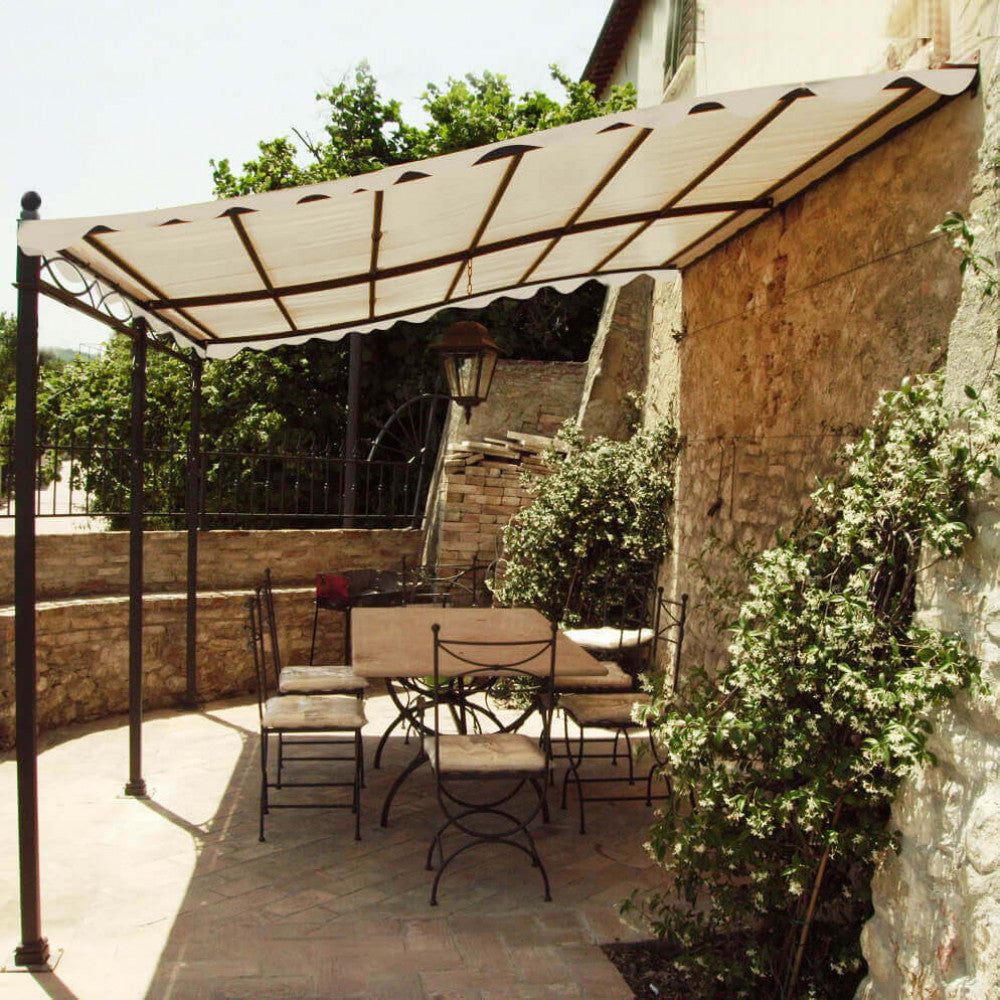 Prospettiva laterale del gazebo pergola addossato in acciaio e poliestere, evidenziando l'integrazione architettonica con la parete in pietra e il pavimento in cotto esterno.