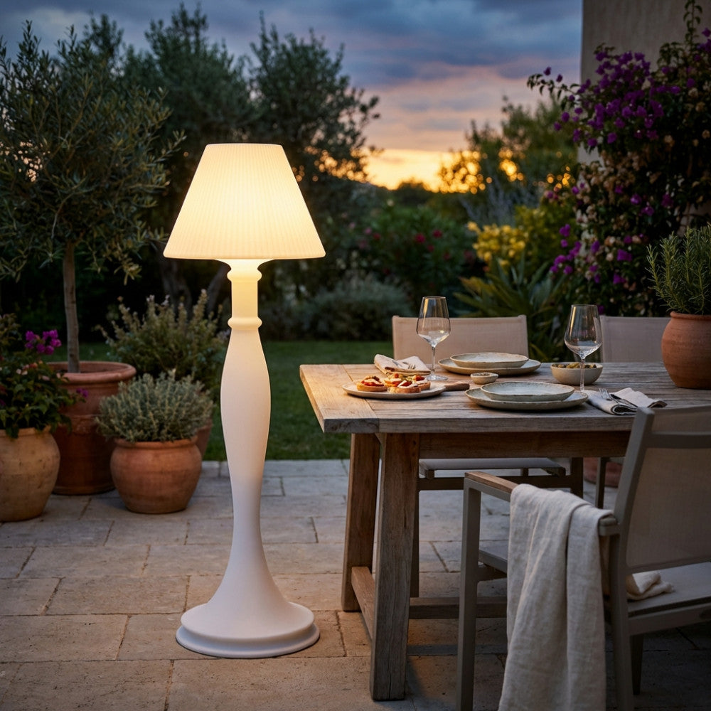 Lampada da terra Aries in polipropilene bianco che illumina un tavolo da pranzo all'aperto al tramonto.