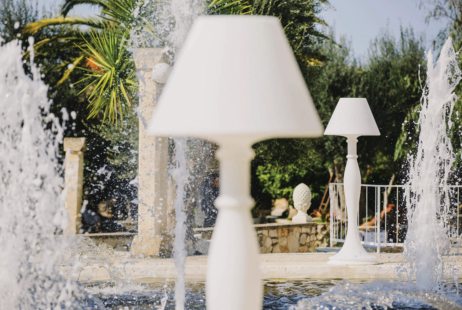 Prospettiva artistica della lampada da terra Aries vista attraverso gli spruzzi d'acqua di una fontana.