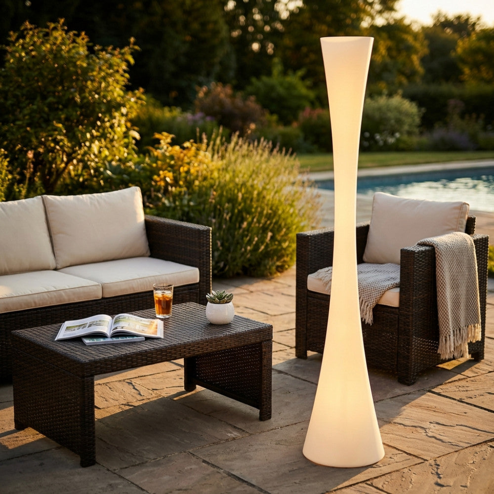 Lampada da terra in polietilene bianco Serpens illuminata in un giardino moderno al tramonto, accanto a divani in rattan.