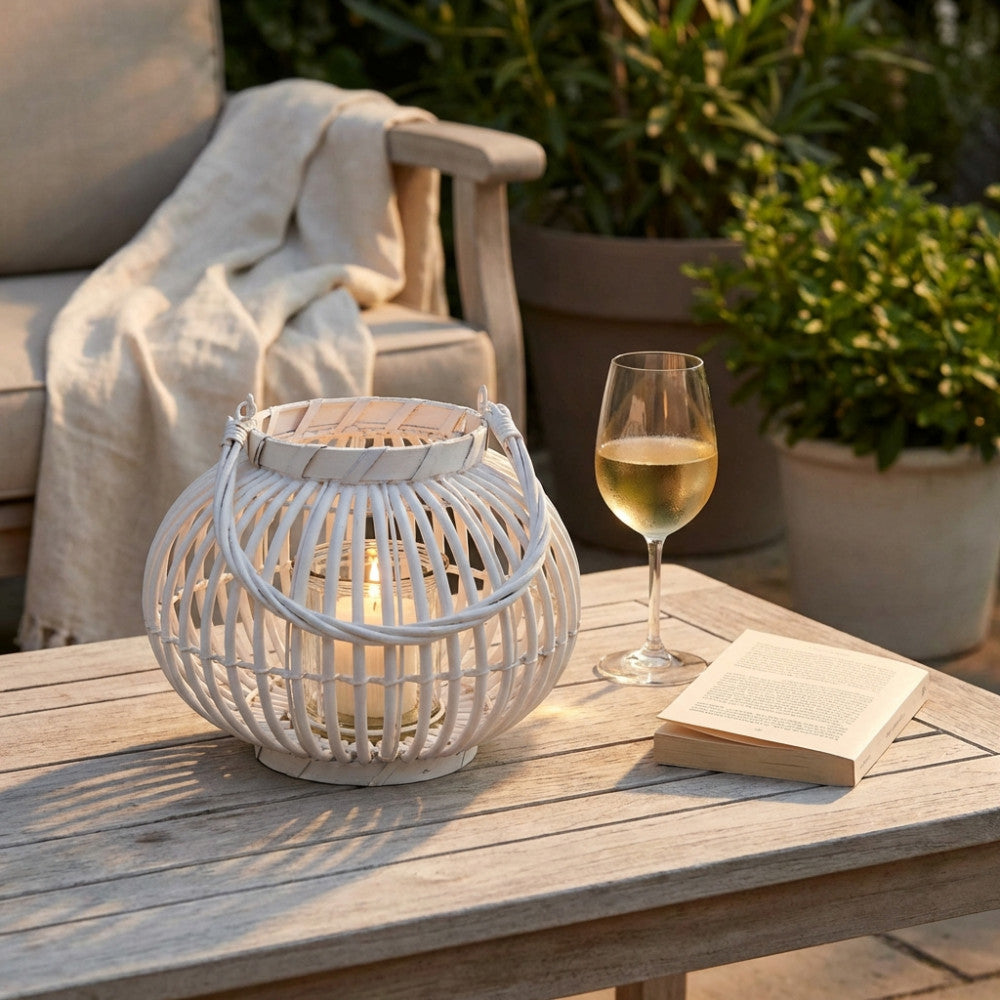 Dettaglio della lanterna intrecciata bianca su un tavolo in teak, accompagnata da un calice di vino e un libro in un patio elegante.