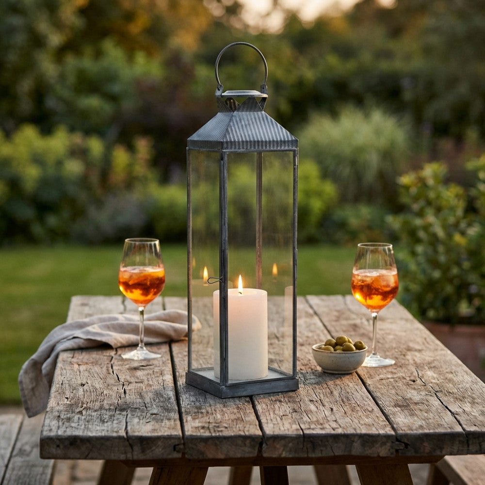 Lanterna Harmony Piccola illuminata su tavolo rustico con calici da aperitivo in giardino.