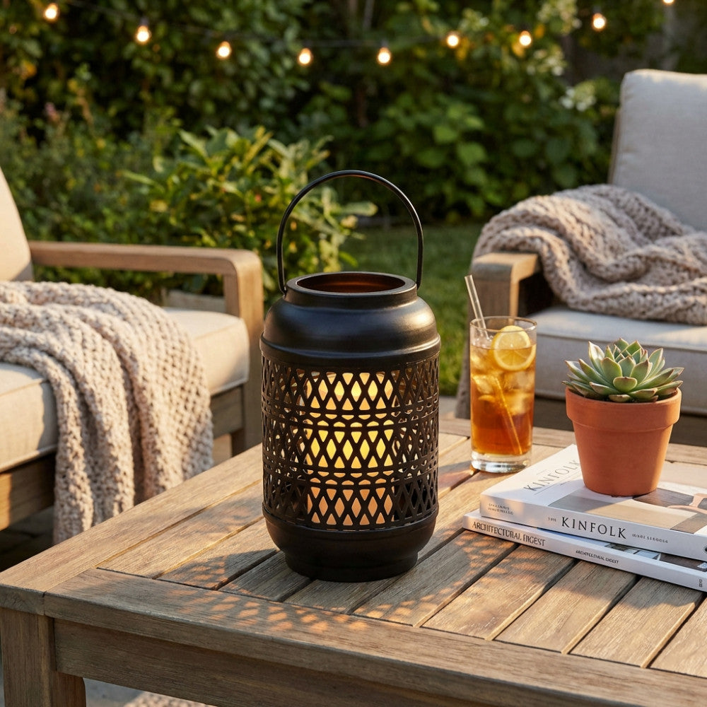 Lanterna in metallo nero illuminata su un tavolo da giardino in legno con piante e bevande.