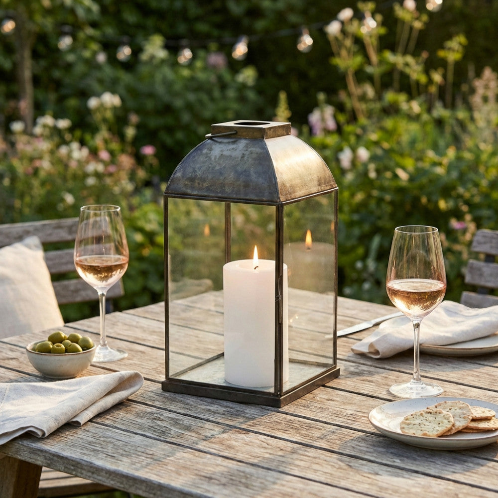 Primo piano della lanterna Karrie Piccola che illumina un allestimento da pranzo all'aperto al tramonto.