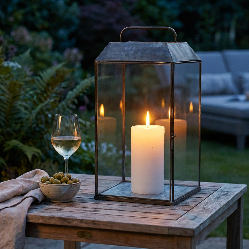 Dettaglio della lanterna illuminata da una candela bianca in un giardino serale, creando un'atmosfera intima.