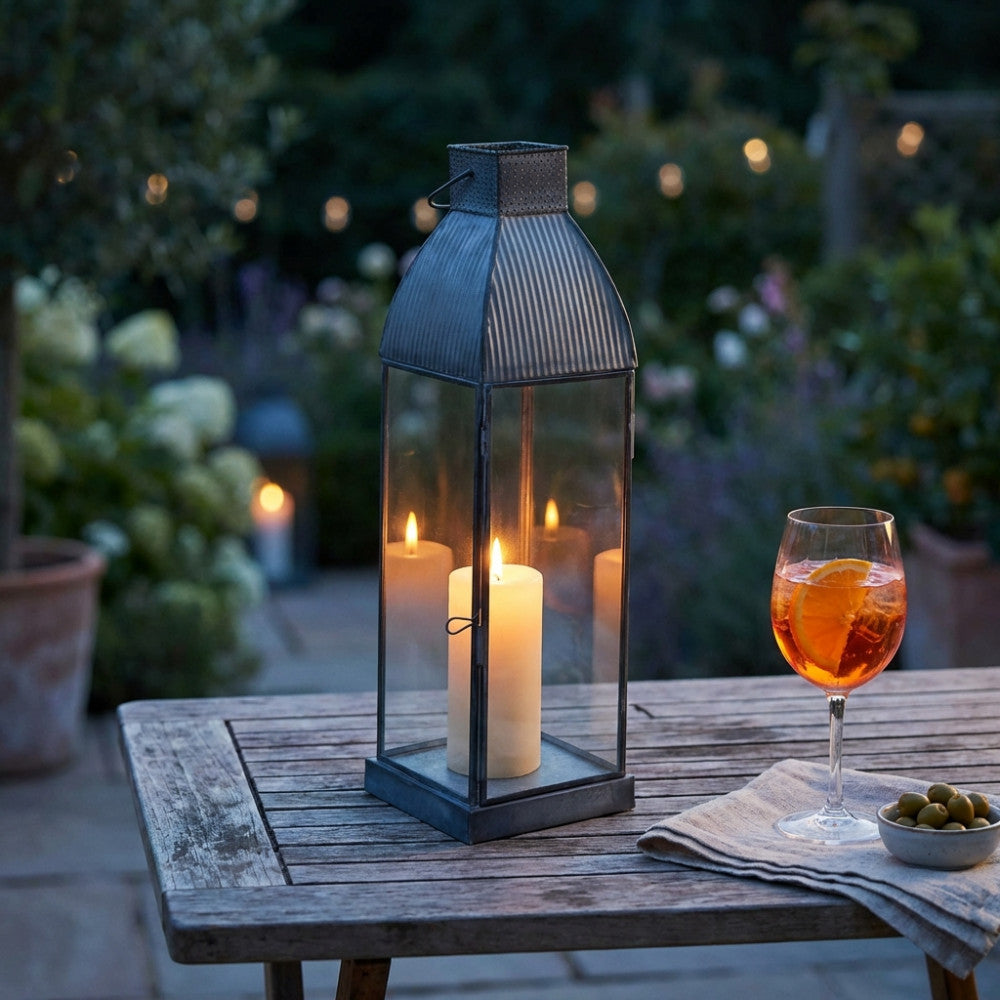 Lanterna Kendra Piccola illuminata da una candela su tavolo da giardino al crepuscolo.