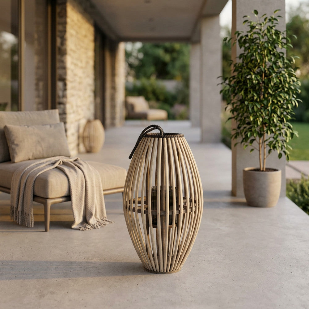 Dettaglio della lanterna in vimini e vetro su una terrazza moderna, illuminata dalla luce naturale del tramonto con piante decorative sullo sfondo.