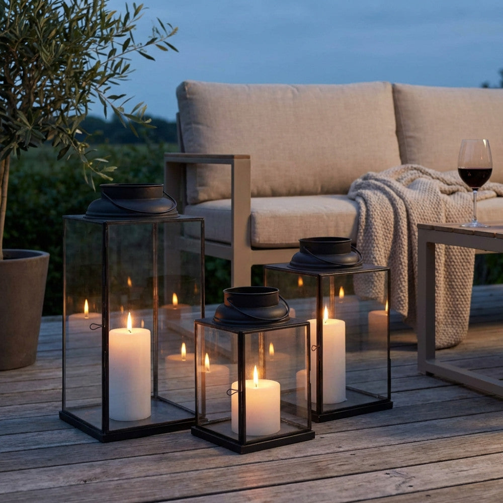 Composizione di lanterne moderne illuminate da candele bianche su una pavimentazione in legno durante le ore serali.