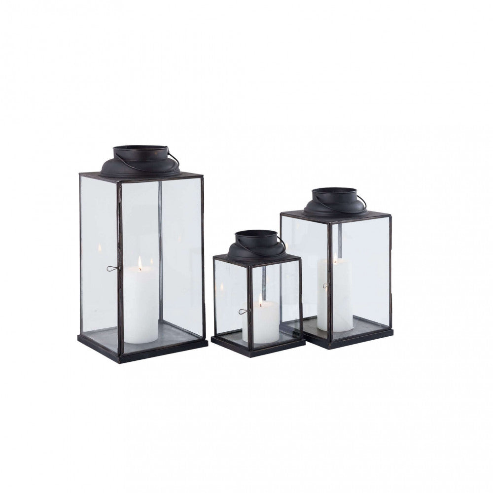 Set di tre lanterne geometriche in acciaio e vetro su fondo bianco, che mostrano le proporzioni e il design minimalista.