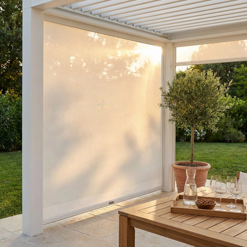 Tenda laterale in textilene bianco per pergola bioclimatica, abbassata per filtrare la luce solare dorata in un giardino curato.