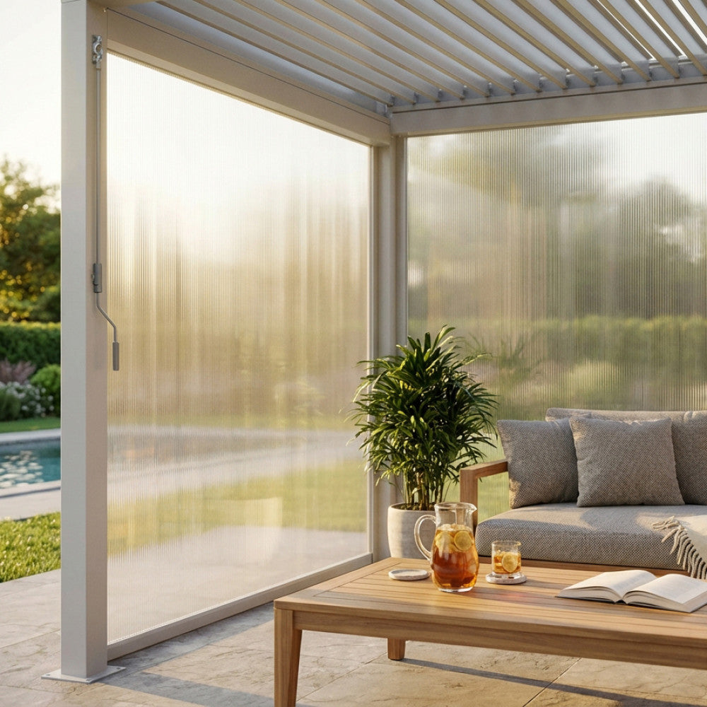 Tenda laterale in PVC bianco per pergola bioclimatica, abbassata per filtrare la luce solare dorata su un salottino outdoor.