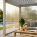 Tenda laterale in PVC bianco per pergola bioclimatica, abbassata per filtrare la luce solare dorata su un salottino outdoor.