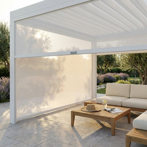 Pergola bioclimatica bianca con pannello laterale in textilene semi-abbassato, che filtra la luce solare su un salotto da esterni in legno.