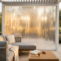 Tenda laterale in PVC per pergola bioclimatica da 4 metri, illuminata dalla calda luce del tramonto con arredi lounge.
