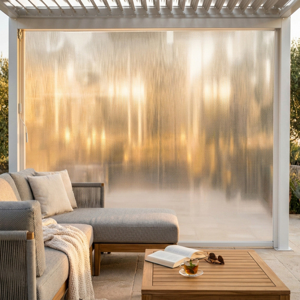 Tenda laterale in PVC per pergola bioclimatica da 4 metri, illuminata dalla calda luce del tramonto con arredi lounge.