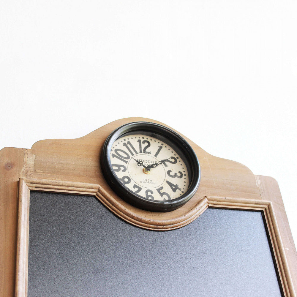 Dettaglio del quadrante analogico dell'orologio in stile vintage, incastonato nella parte superiore della cornice in legno sagomato.
