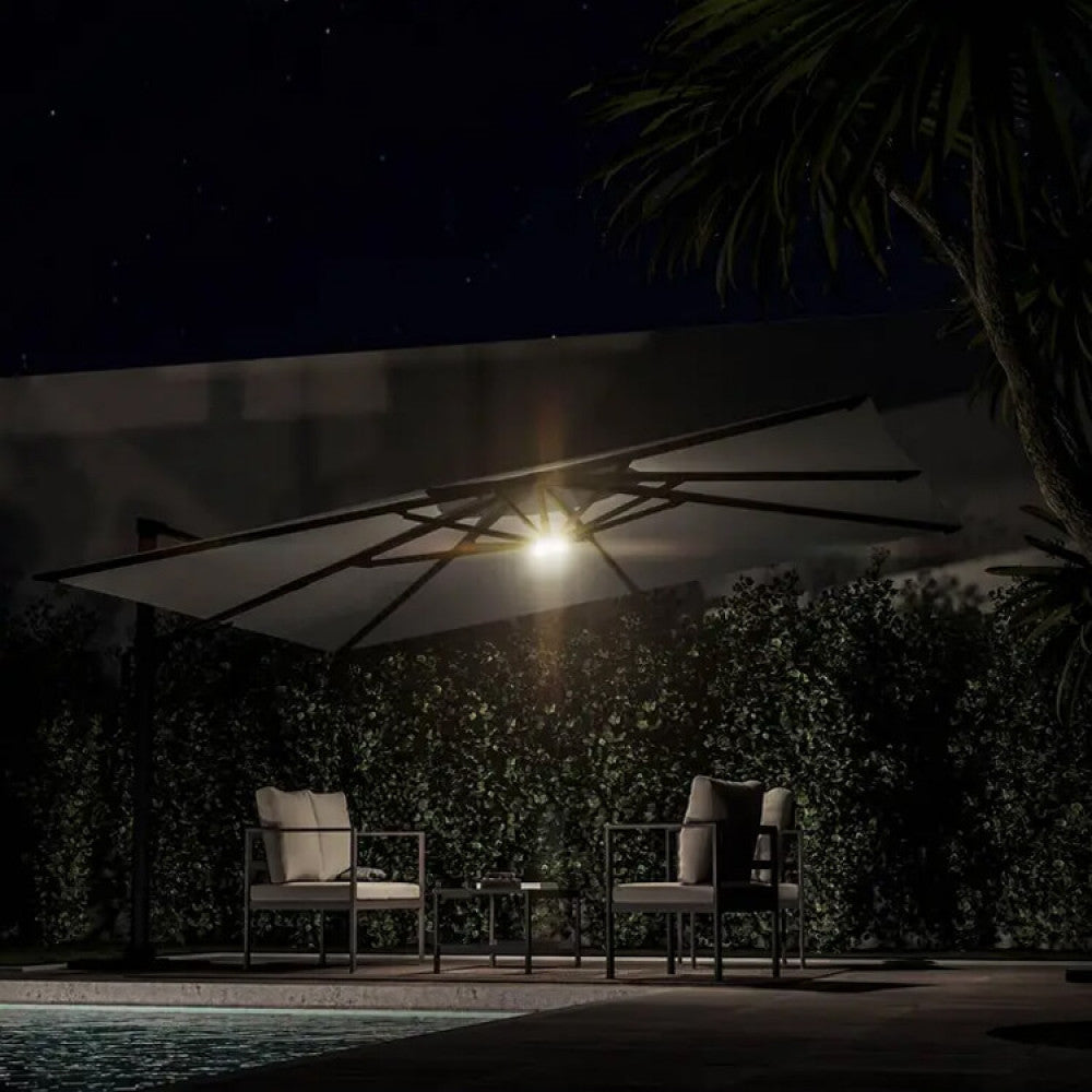Area lounge esterna notturna splendidamente illuminata dalla luce LED per ombrellone Newton, creando un'atmosfera serena.
