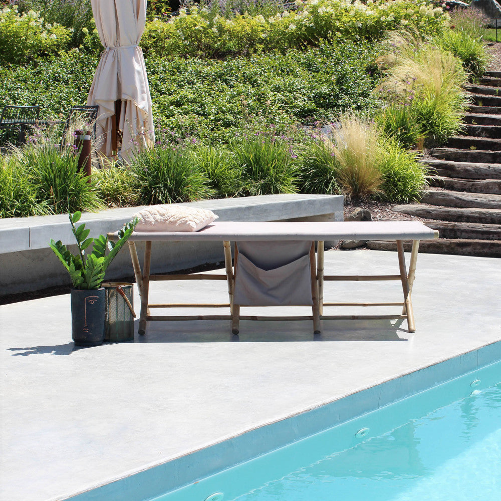 Lettino prendisole in legno inserito in un contesto outdoor moderno con piscina e vegetazione mediterranea.