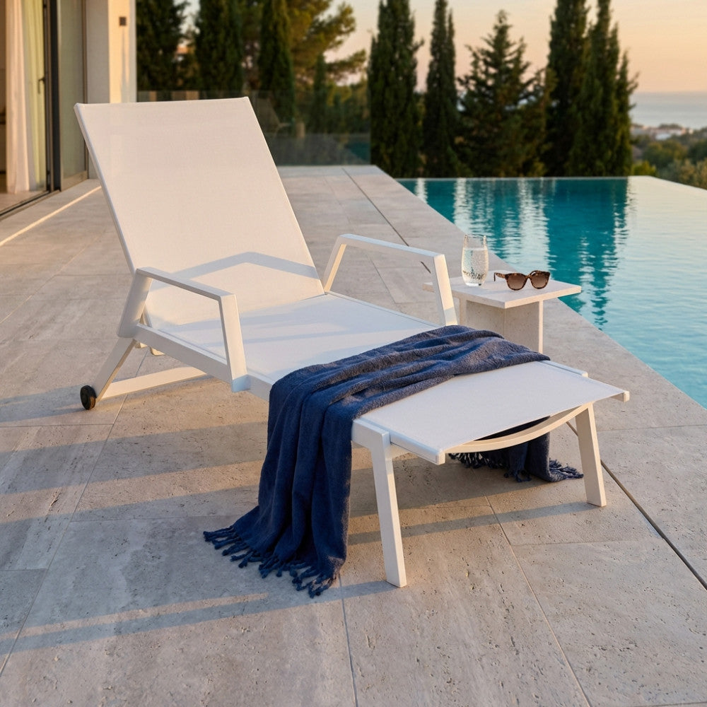 Lettino prendisole Barinas bianco con asciugamano blu e tavolino in cemento a bordo piscina.