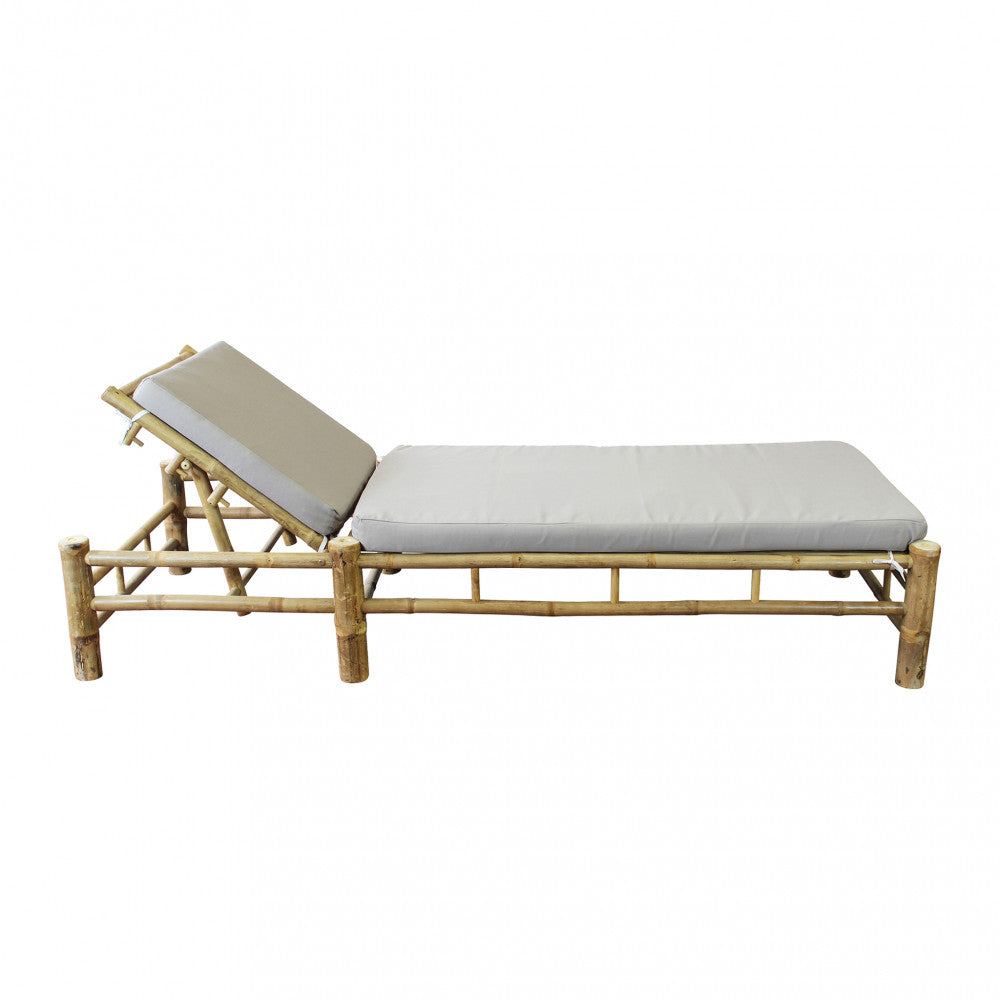 Lettino prendisole Blue Lagoon in bamboo di colore marrone con cuscino, posizionato in un giardino lussureggiante.