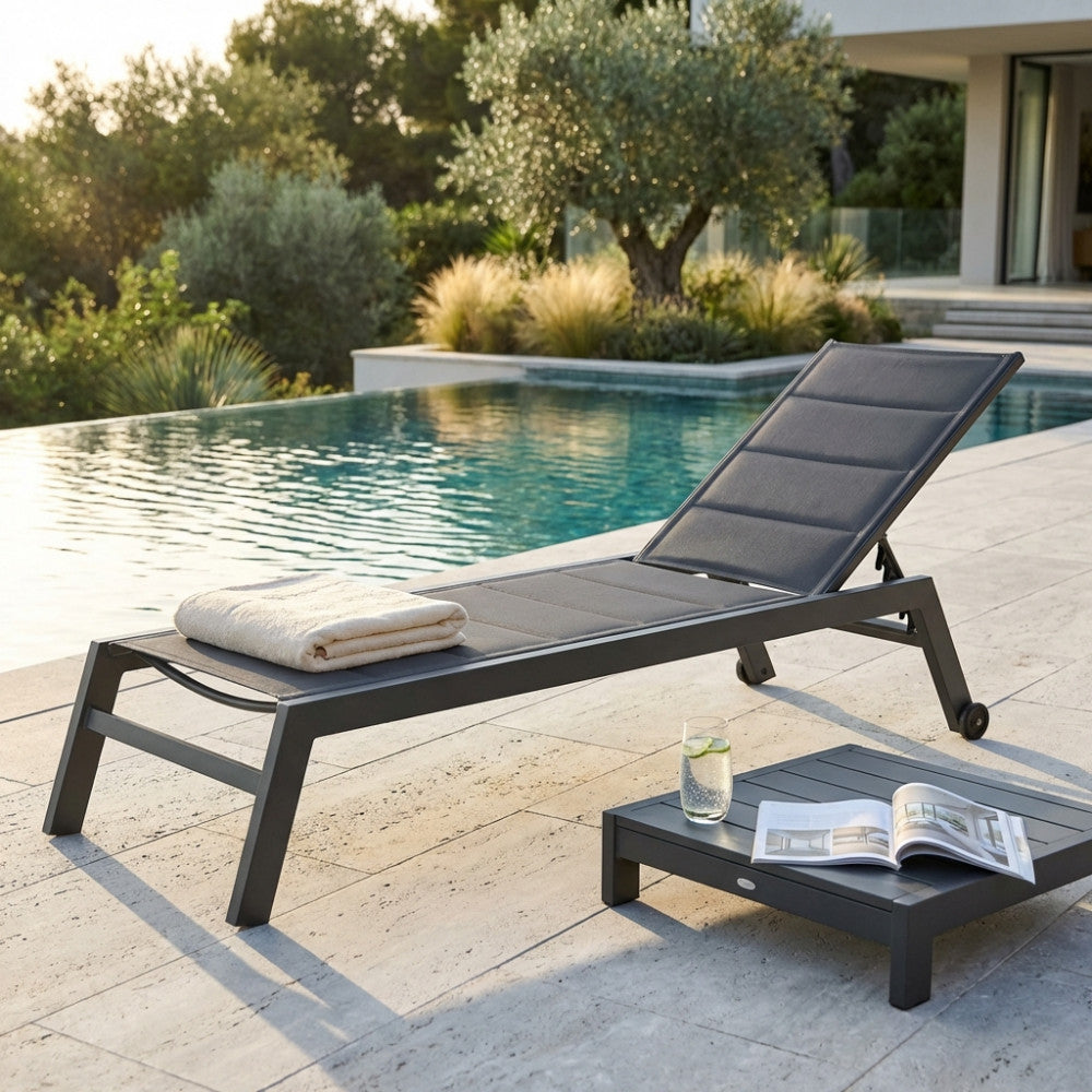 Lettino prendisole Formentera in alluminio antracite posizionato a bordo piscina con asciugamano e tavolino.