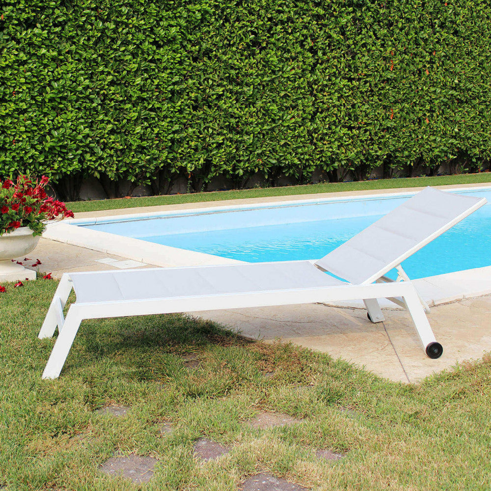 Lettino da giardino posizionato su prato verde accanto a una piscina con siepe sullo sfondo.