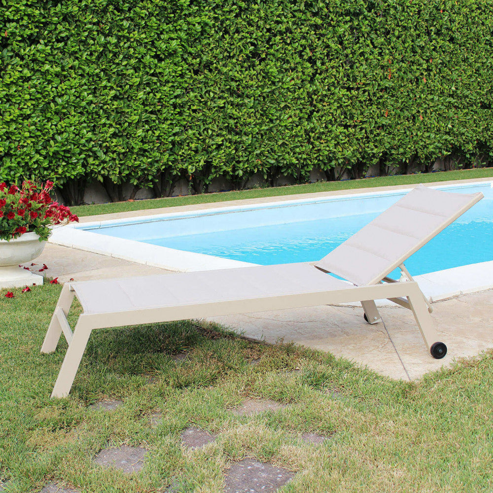 Lettino prendisole Formentera inserito in un giardino curato con prato verde e piscina, mostrando la sua eleganza geometrica.