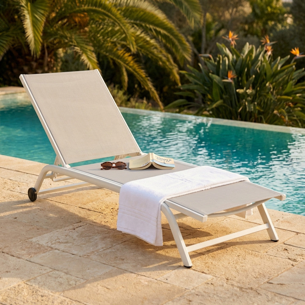 Lettino prendisole Itaca in alluminio bianco e textilene posizionato a bordo piscina, arricchito da un asciugamano e un libro.