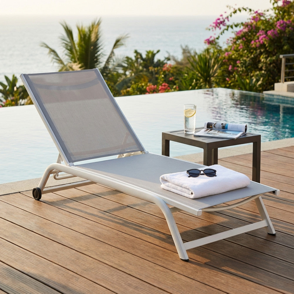 Lettino Itaca dal design moderno su una terrazza in legno con vista mare, affiancato da un tavolino minimalista.