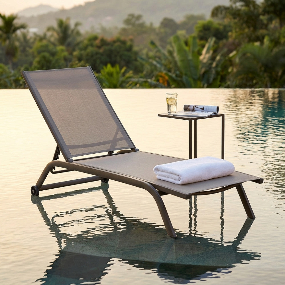 Lettino outdoor Itaca immerso nell'acqua bassa di una piscina a sfioro con tavolino laterale e vista panoramica.